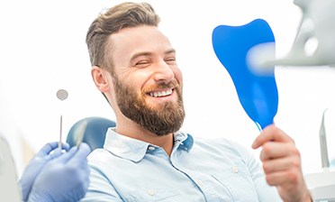 bearded dental patient admiring his new smile in a mirror
