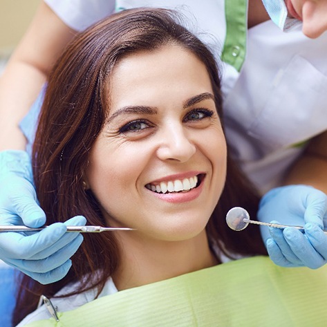 Woman smiling at camera while dentist conducts oral exam