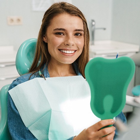 Young woman in blue shirt smiling while holding tooth-shaped mirror