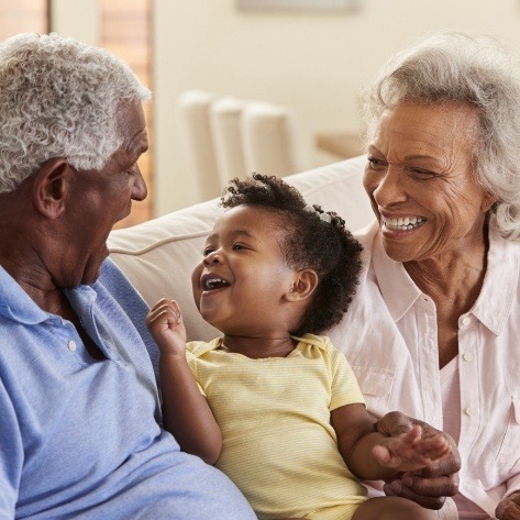 Grandchild smiling with grandparents as they enjoy the benefits of dental implants