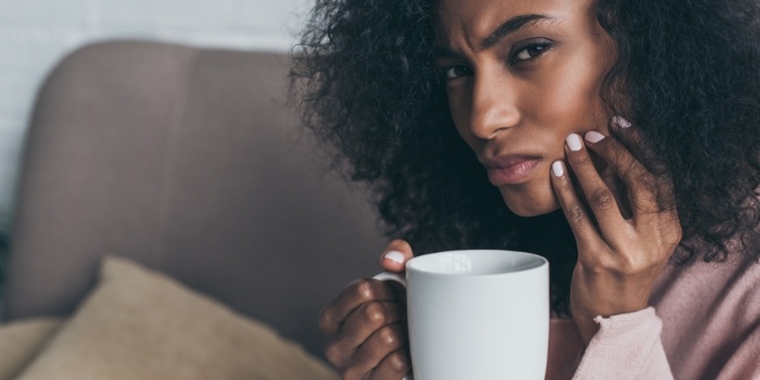 Woman with white coffee mug holding her cheek in pain
