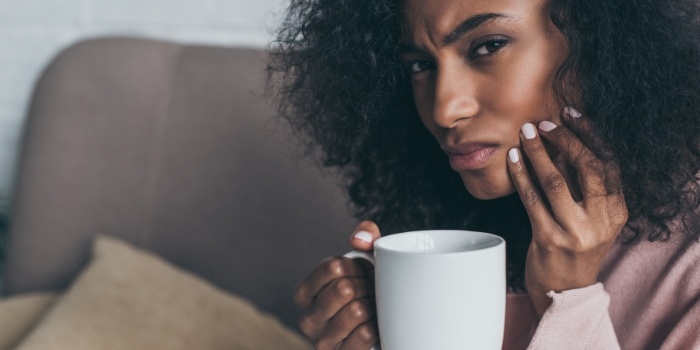 Woman holding white coffee mug and touching her cheek in pain