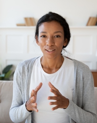 Woman wearing gray cardigan sitting on couch and gesturing with her hands