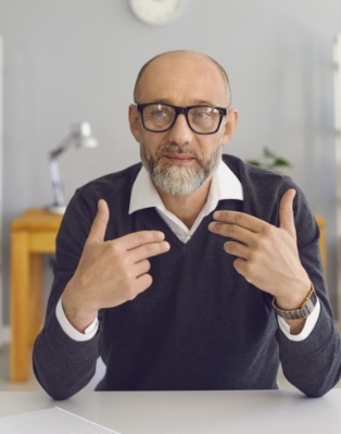 Man in black sweater sitting at table and pointing to himself