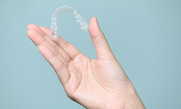 Patient holding Invisalign aligner against blue background