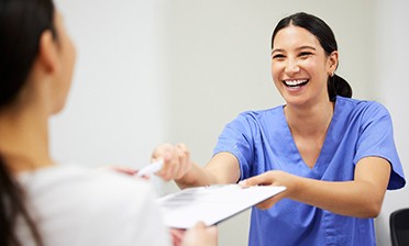 Dental assistant smiling while handing patient form