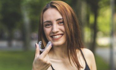 Smiling woman holding an Invisalign clear braces tray