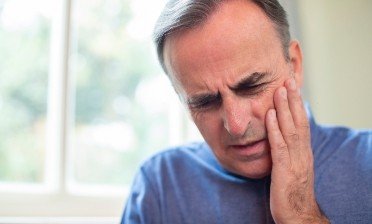 Man in need of emergency dentistry holding cheek in pain