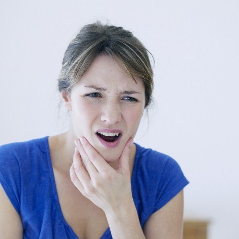 Woman in need of TMJ therapy holding jaw in pain