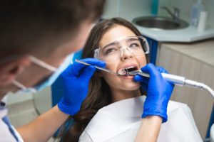 Woman with brown hair getting a root canal done by a dentist wearing blue gloves